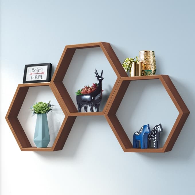 Set of three walnut hexagon wall shelves holding plants, frames and decor