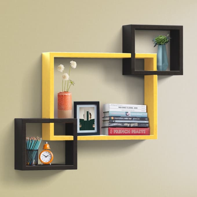 Yellow and black interlocking square wall shelves holding books, a frame and a vase